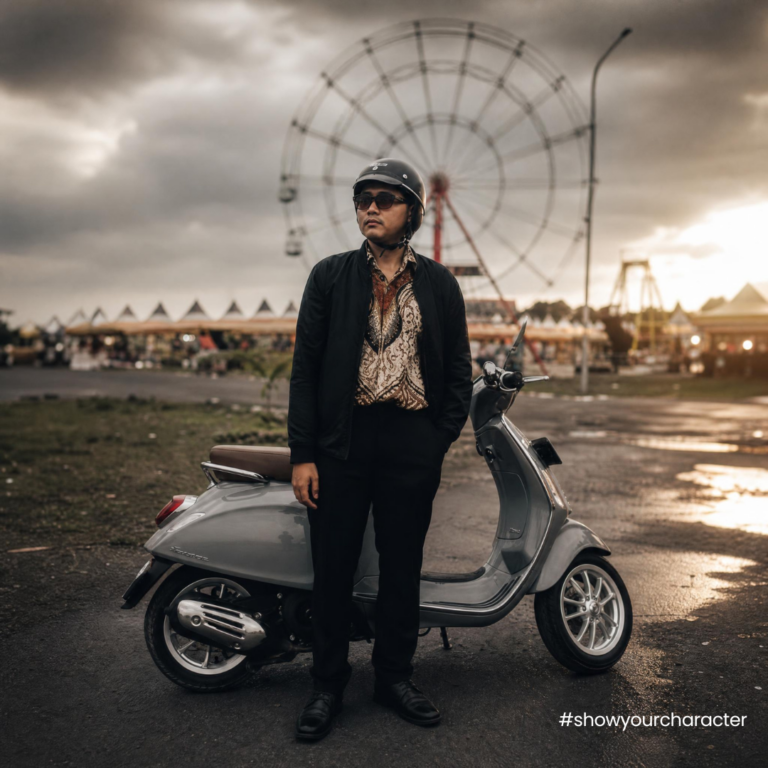 Pengendara berkemeja batik berdiri di samping Vespa saat matahari terbenam